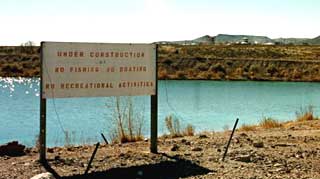 A pond near the firing range. No construction is anywhere to be seen, but the sign says: UNDER CONSTRUCTION NO FISHING, NO BOATING NO RECREATIONAL ACTIVITIES (Socorro, New Mexico)