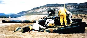 Investigation: These US soldiers are investigating radioactive contamination and potential protective measures after firing DU shells at this Iraqi tank brought to the US as a "spoil of war." They are wearing protective clothing and masks to prevent contamination. (Courtesy of Douglas Rokke, taken June 1995, at the nuclear test site in Nevada)